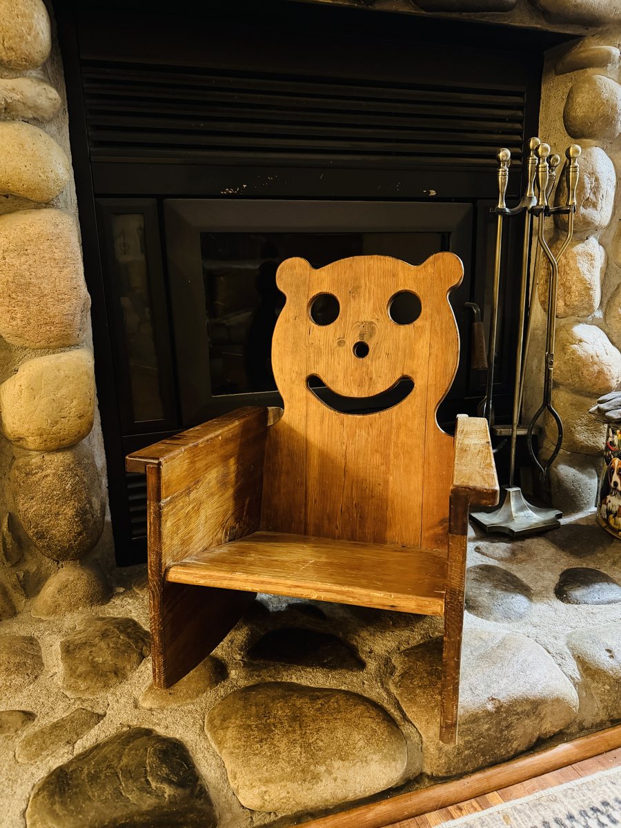 A child-sized wooden chair with a smiling bear-face back, on a river-rock hearth
